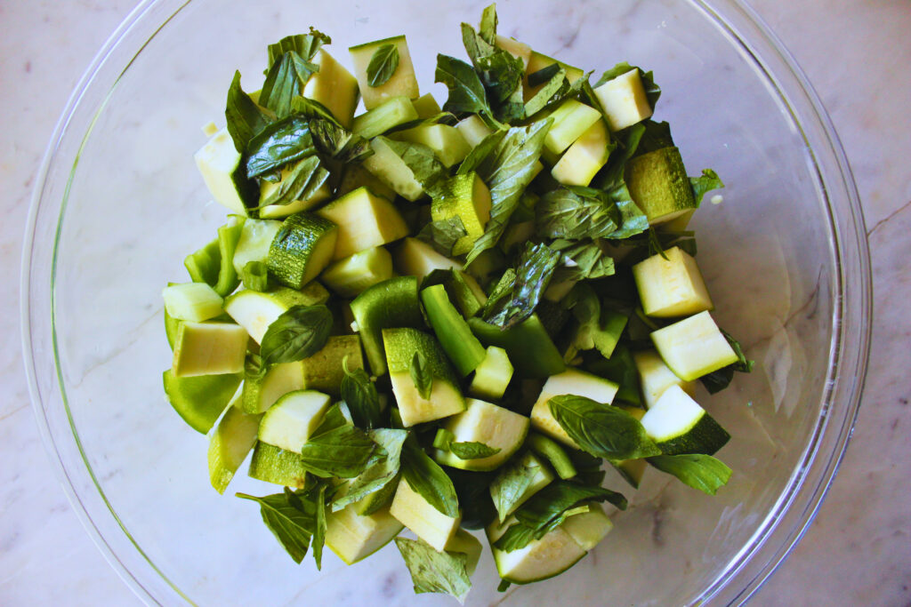 overhead image of a glass bowl with chopped ingredients for green gazpacho recipe